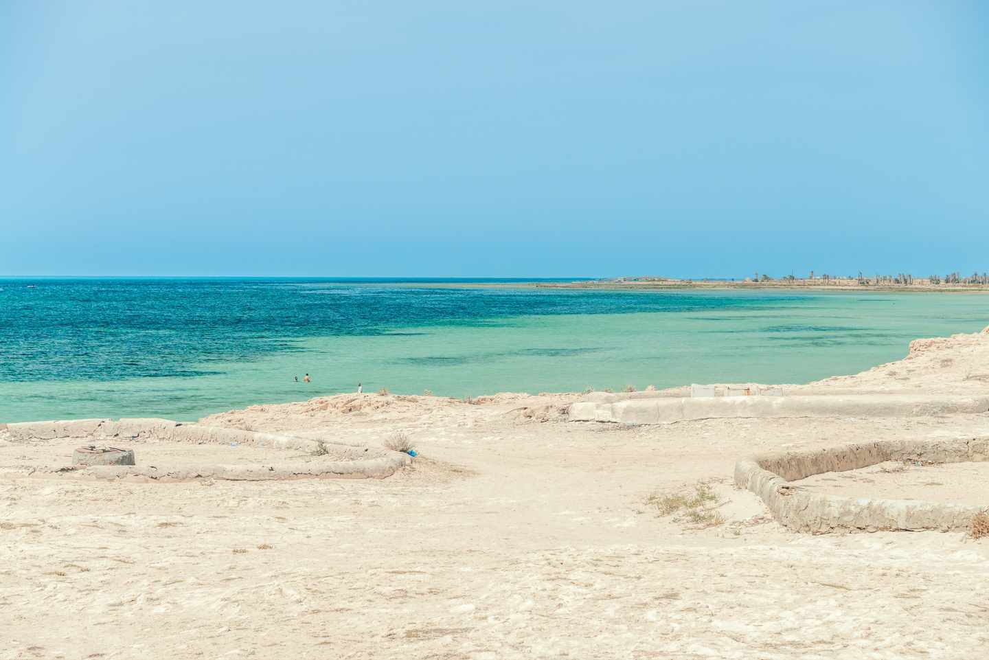 Heller Sandweg führt zu einem flachen türkisfarbenen Küstenabschnitt mit ruhigem Meer auf Djerba in Tunesien