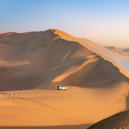 Gerade Schotterstraße durch goldene Savanne mit den markanten Felsbergen der Spitzkoppe am Horizont in Namibia