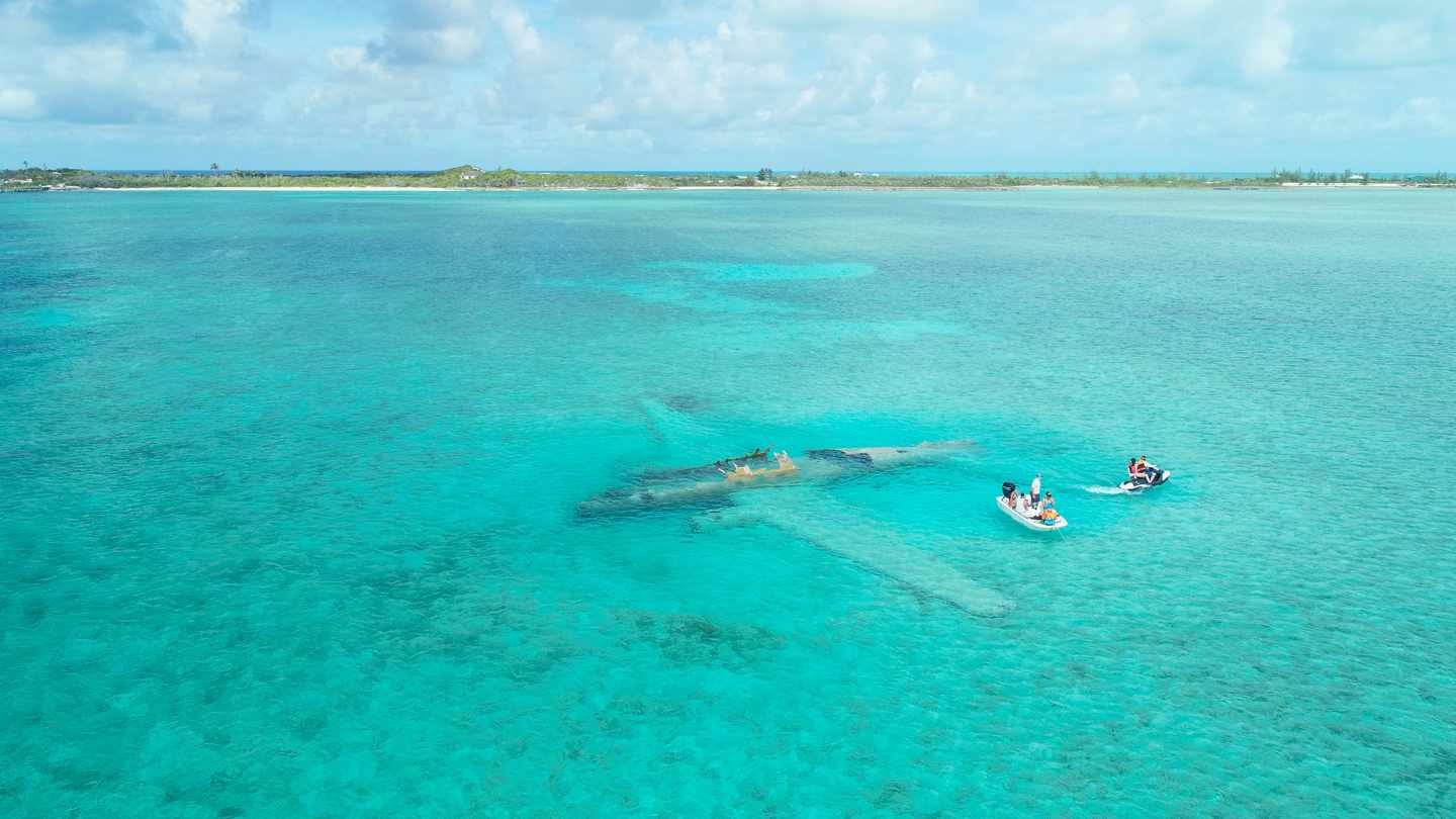 Luftaufnahme des Flugzeugwracks in Exumas Bahamas neben einem Jetski und einem Boot