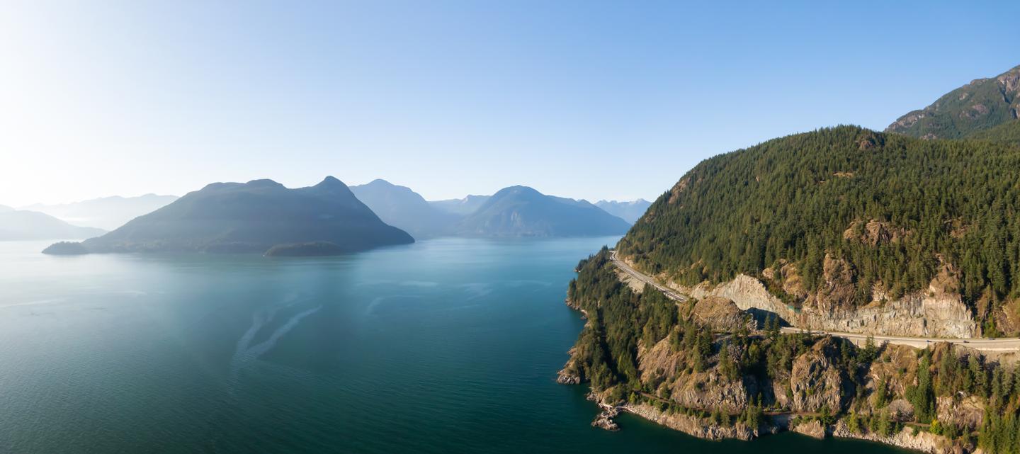 Luftaufnahme des Sea to Sky Highway am Howe Sound mit bewaldeten Bergen und Küste in British Columbia