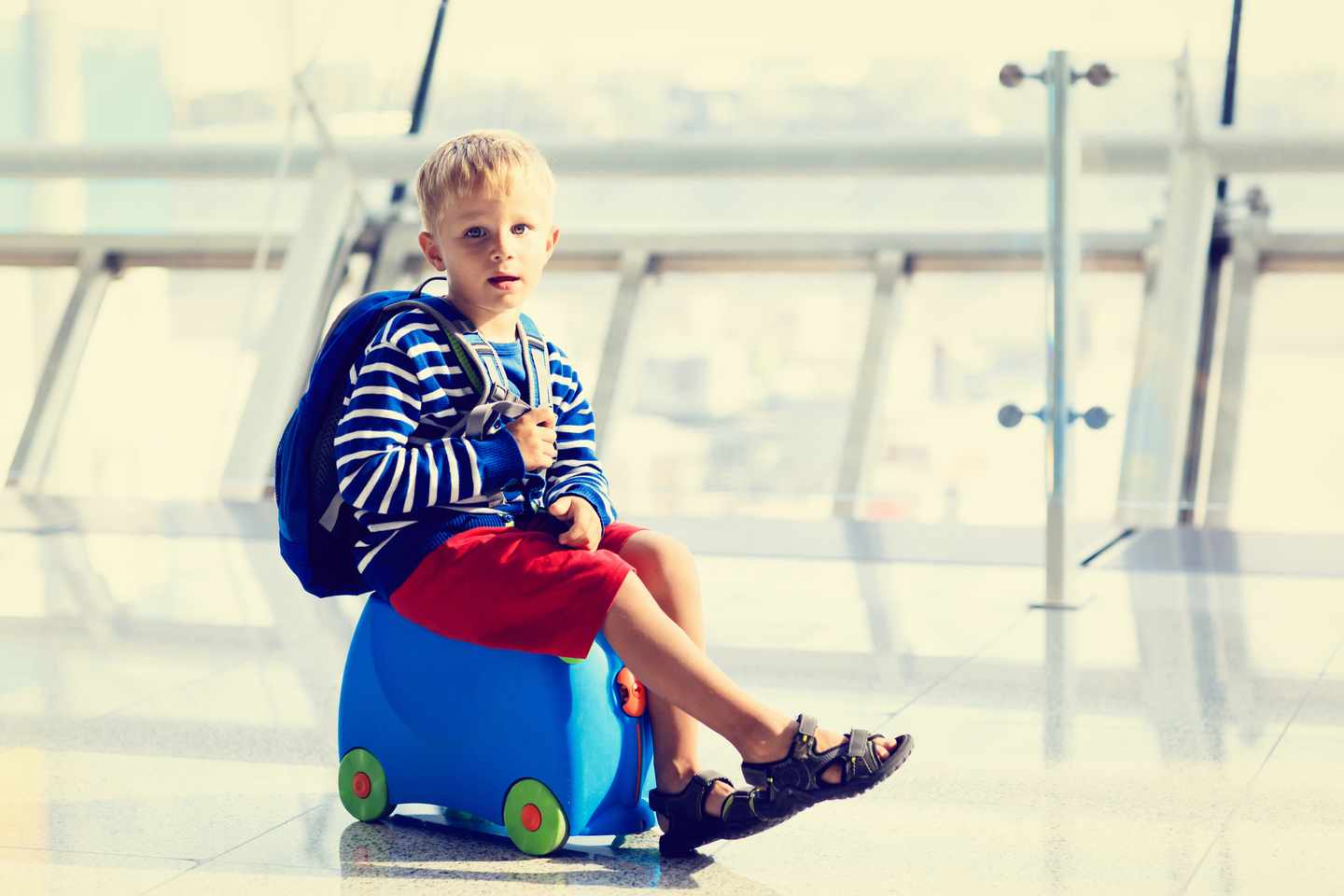 blt46b73c3f481bdd28-kinder-fliegen-flughafen-junge-koffer-g-493657448.jpg Junge sitzt auf blauem Koffer im Flughafen