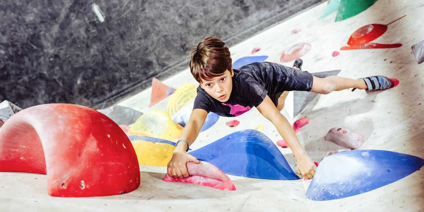 familienurlaub-junge-an-kletterwand-in-boulderhalle-g-1295043364.jpg