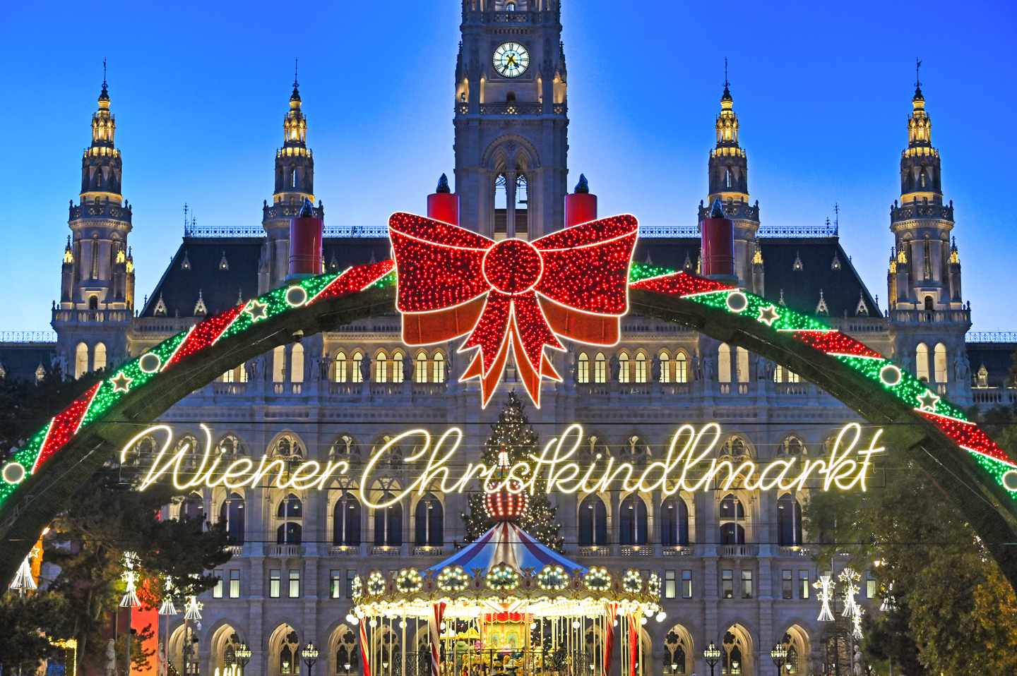 Beleuchteter Eingang zum Wiener Christkindlmarkt mit Karussell und Rathaus im Hintergrund