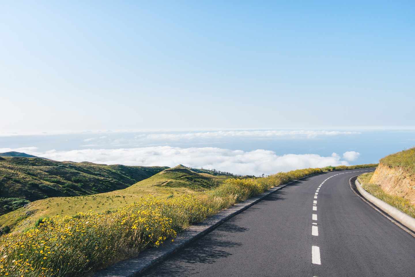 Bergstraße auf Madeira mit blühenden Hängen, Wolkenmeer und weiter Aussicht über die Berglandschaft Portugals