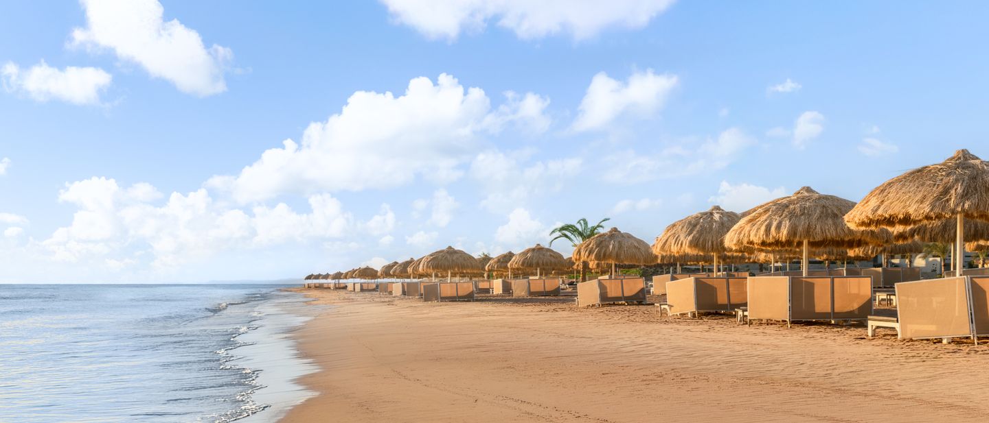 Breiter Sandstrand mit Strohschirmen und Liegen am Roten Meer in El Gouna, Ägypten