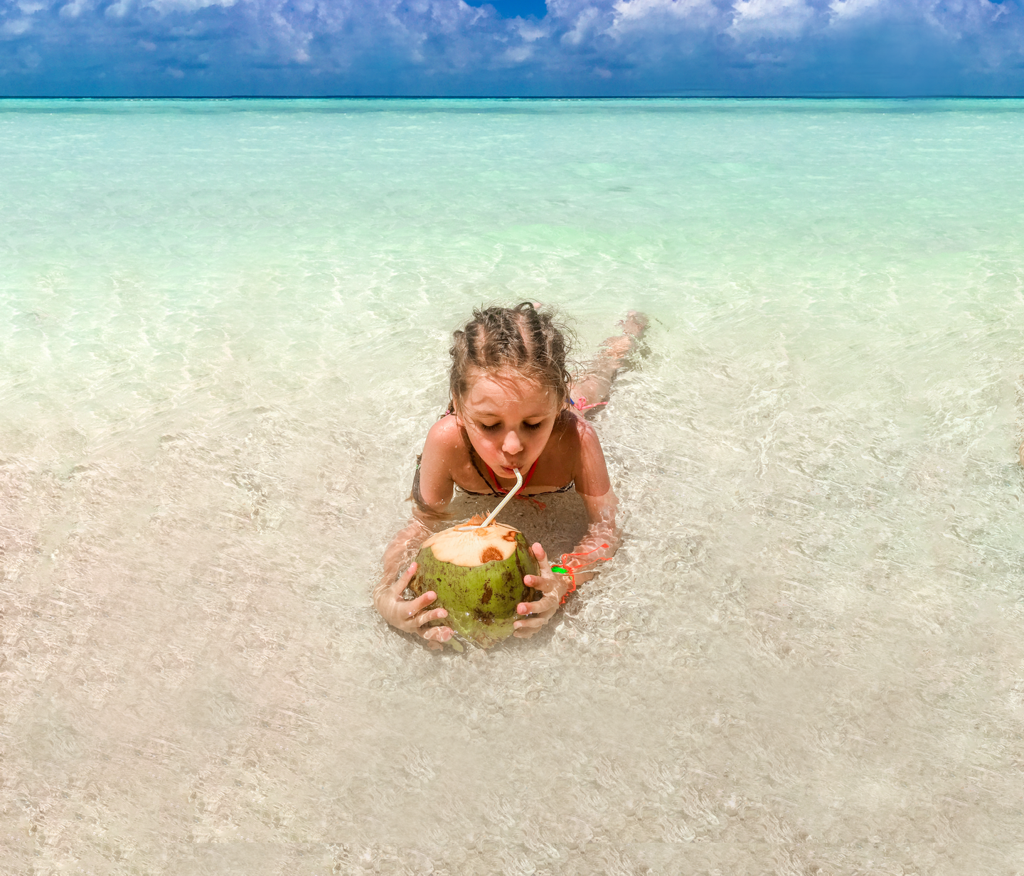 malediven-maedchen-mit-kokosnuss-in-der-hand-liegt-im-seichten-wasser-g-665613966.png