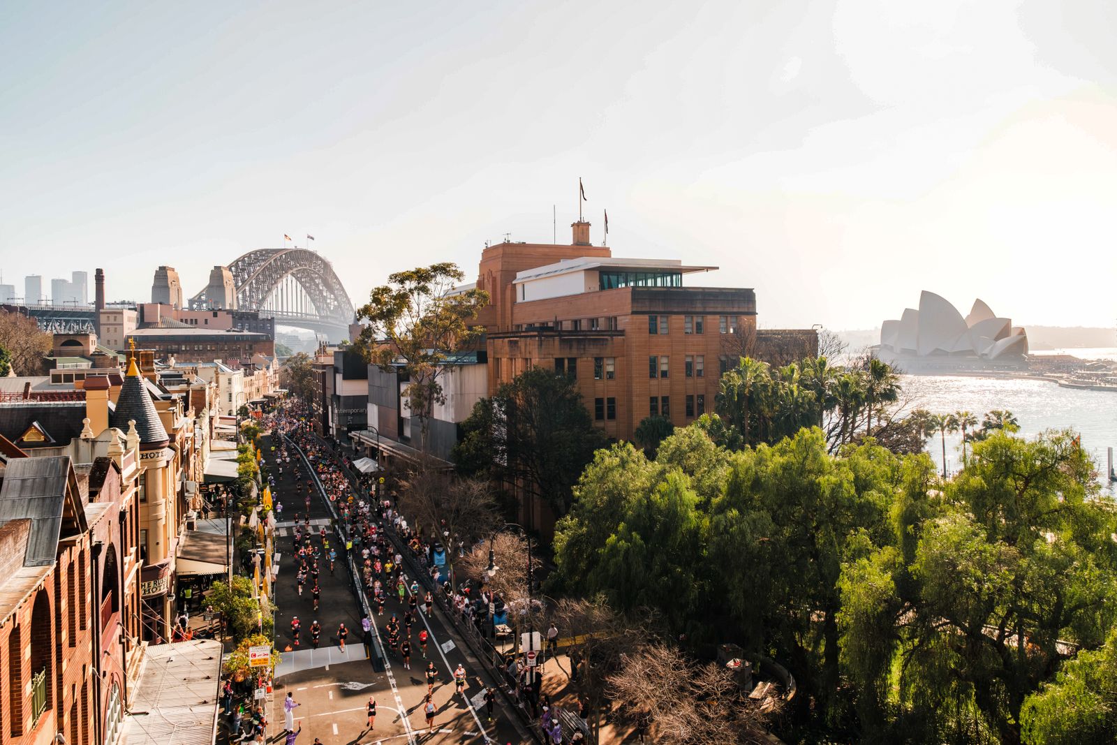 Blick auf Straße in Sydney beim Marathon mit Läufern und im Hintergrund ist die Harbour Bridge und das Opernhaus in weiß zu sehen.