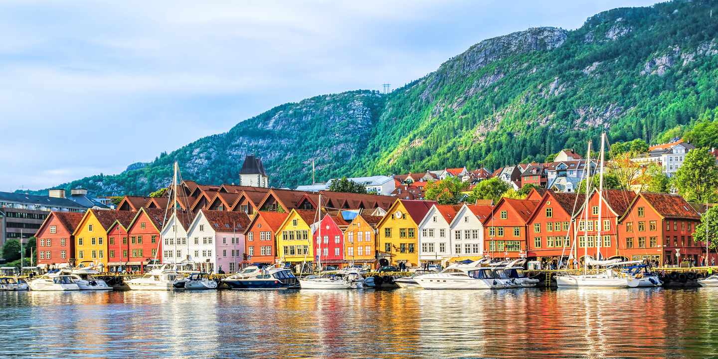 Bunte historische Holzhäuser am Hanseviertel Bryggen mit Hafen und Booten vor den Bergen von Bergen, Norwegen