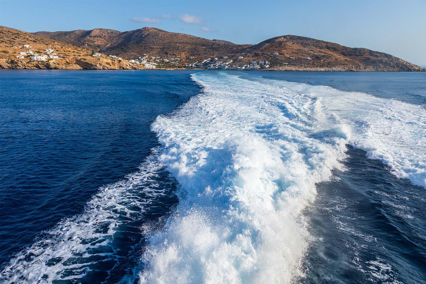 Weiße Wellen hinter einem Boot im blauen Meer mit Bergen im Hintergrund