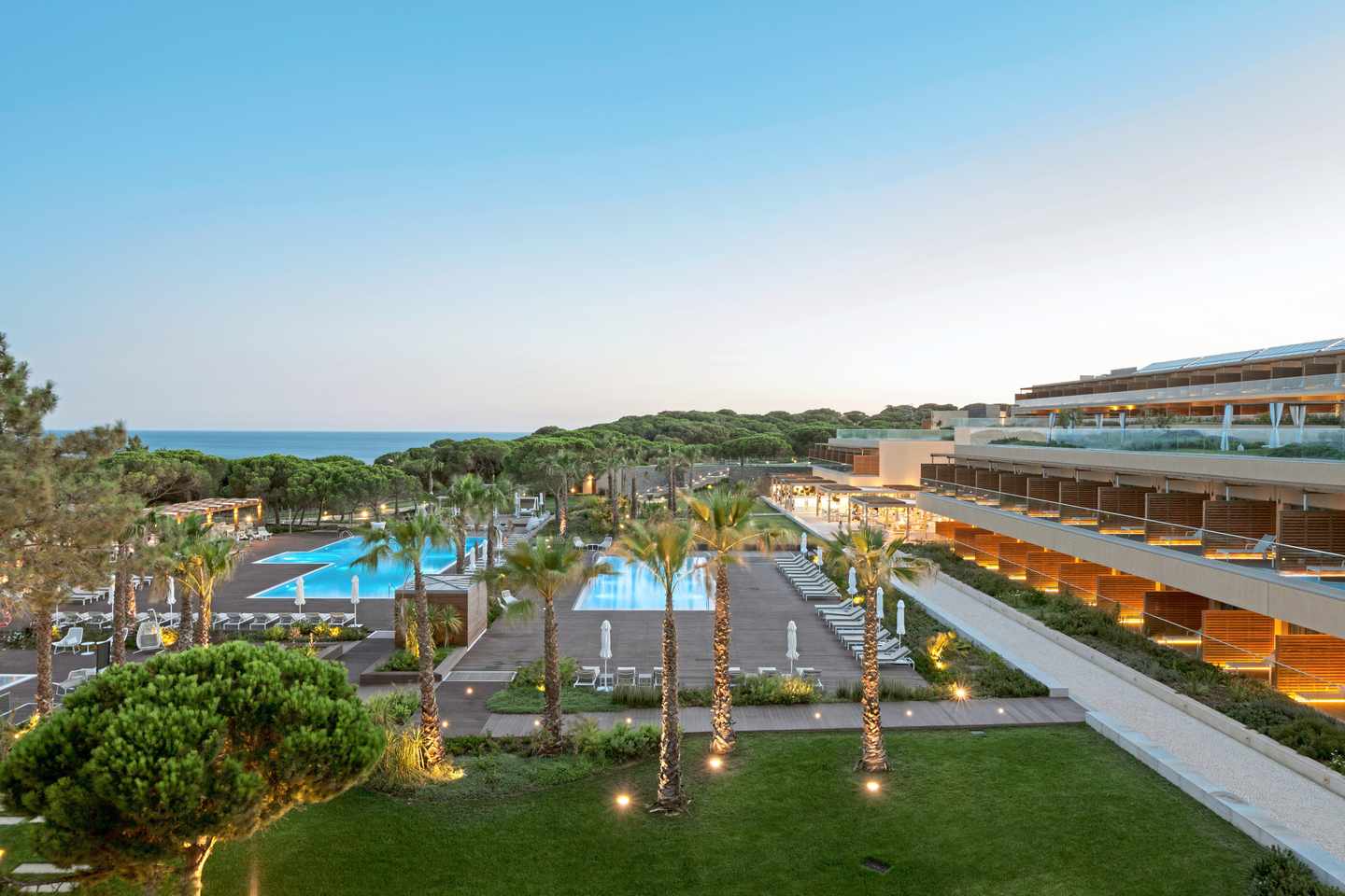 Poollandschaft des EPIC SANA Algarve mit Palmen, modernen Gebäuden und Pinienwald nahe der Atlantikküste bei Olhos de Água