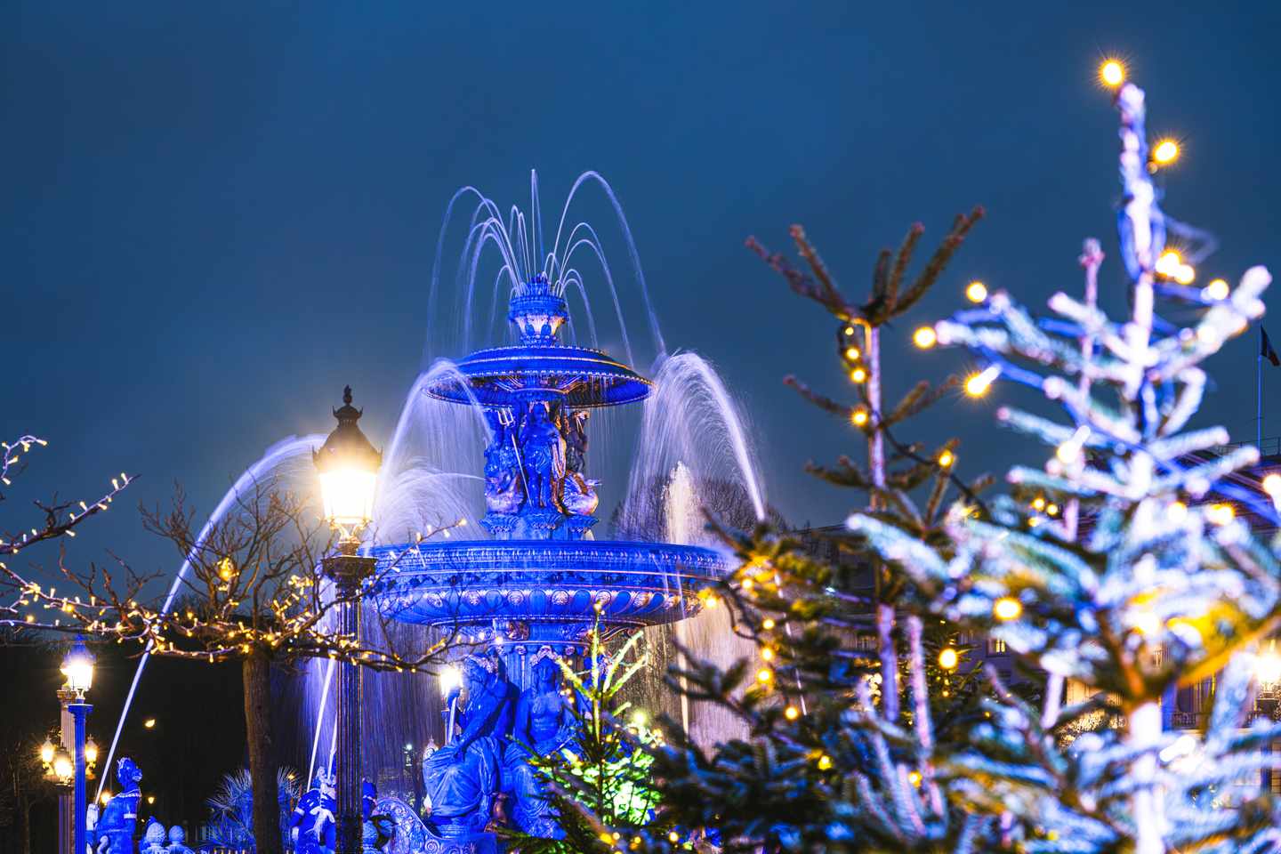 Beleuchteter Brunnen an der Place de la Concorde in Paris mit weihnachtlich geschmückten Bäumen