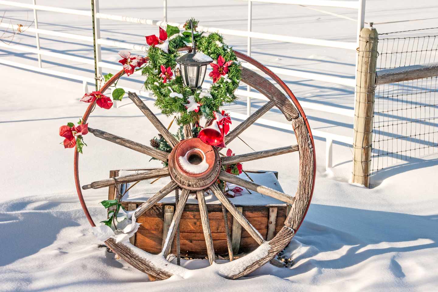 Altes Wagenrad im Schnee mit Laterne, grünem Weihnachtskranz und roter Dekoration