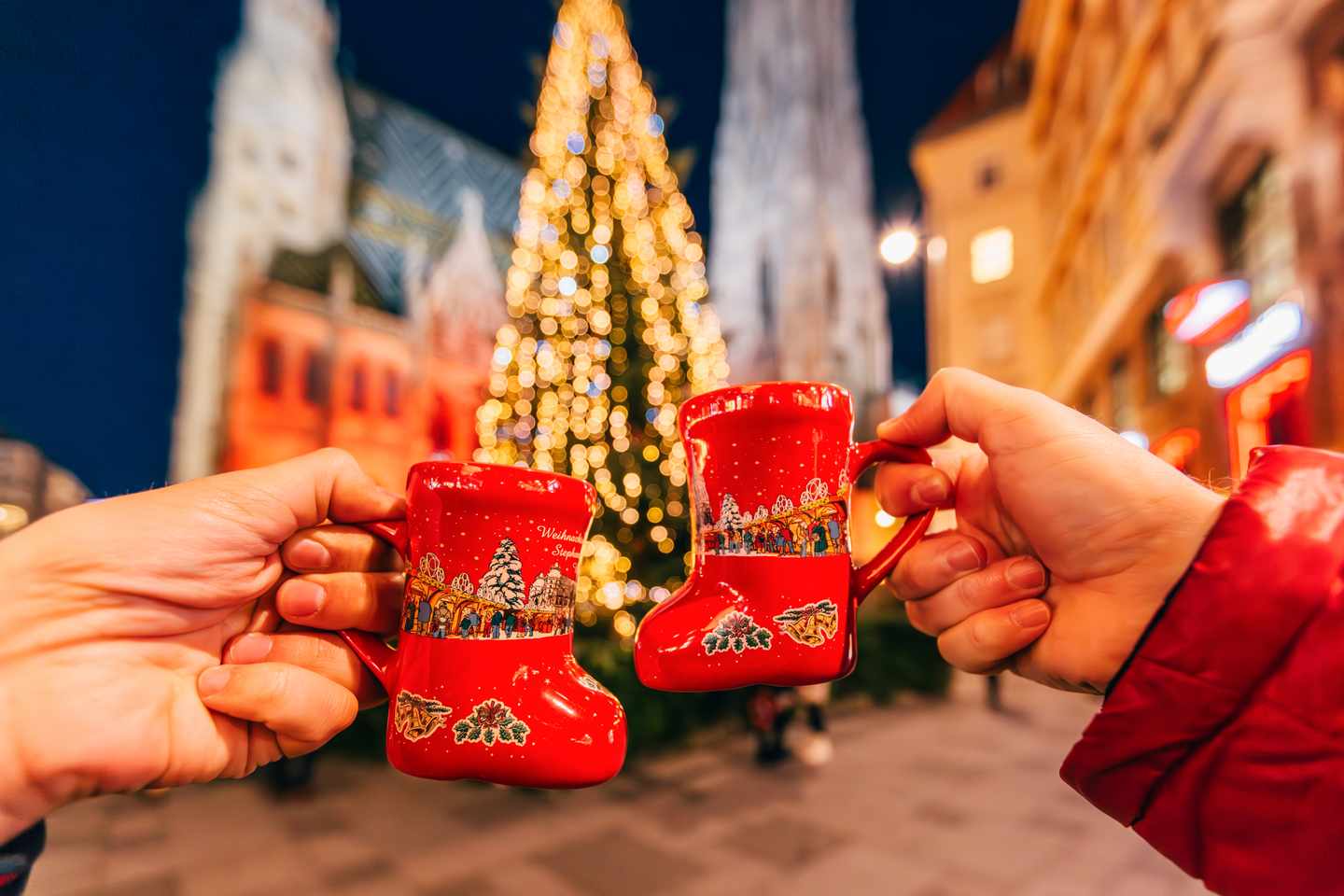 Zwei rote Glühweinbecher vor beleuchtetem Weihnachtsbaum auf einem Wiener Weihnachtsmarkt
