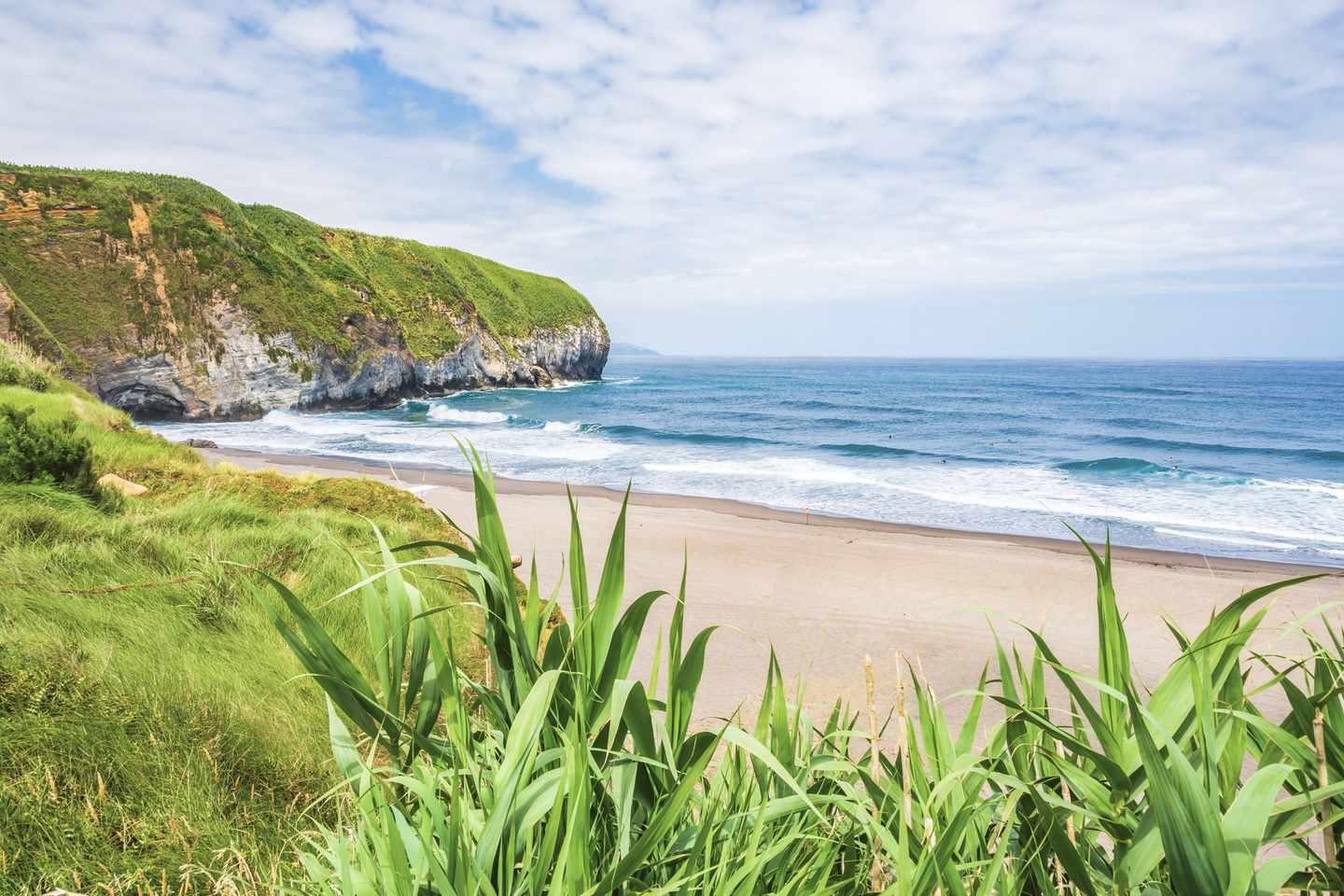 Schwarzer Sandstrand der Praia de Santa Bárbara auf São Miguel mit grünen Klippen am Atlantik