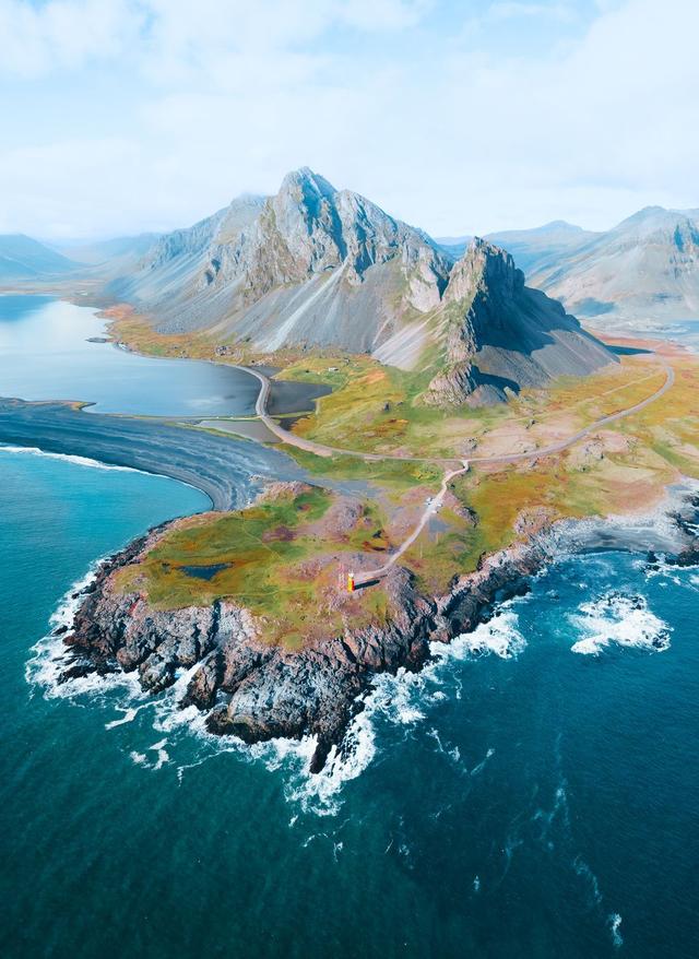 Island Urlaub Luftaufnahme von einer beeindruckenden Island Landschaft mit zerklüfteter Küste, tiefblauem Meer und markanten Bergen im Hintergrund