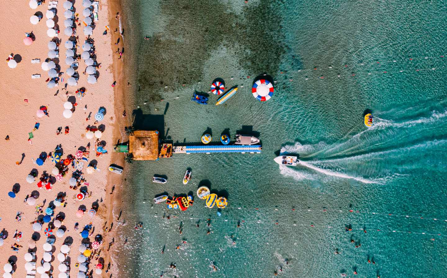 GettyImages-1154728449.jpg Luftaufnahme eines Strandes mit bunten Sonnenschirmen  Liegen  einem Steg und Booten