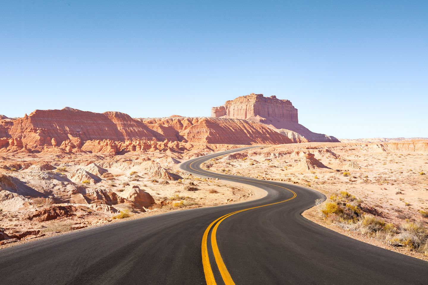Geschwungene Straße mit gelben Mittellinien führt durch eine karge Felslandschaft unter klarem Himmel