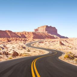Geschwungene Straße mit gelben Mittellinien führt durch eine karge Felslandschaft unter klarem Himmel