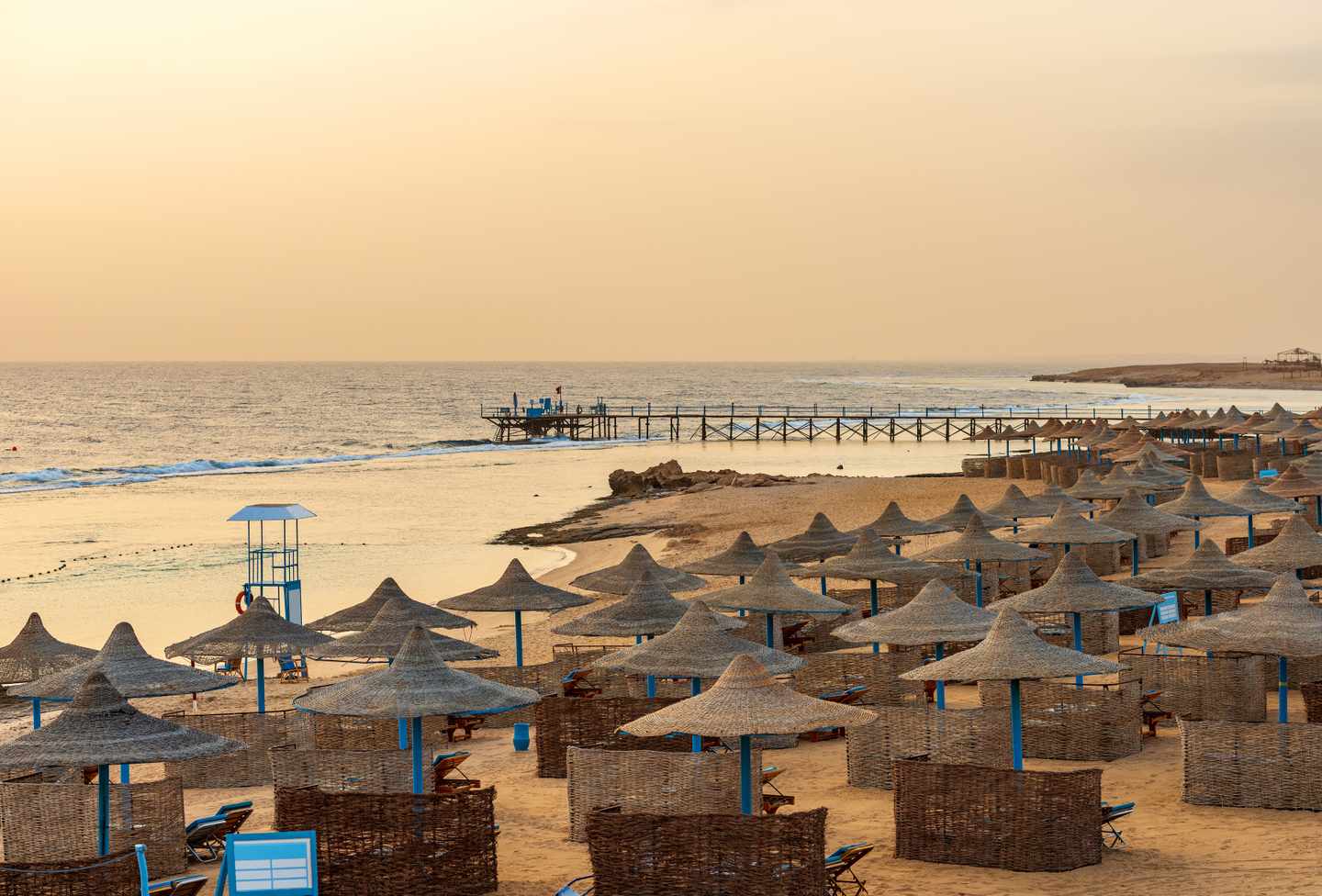 Leerer Sandstrand in der Nähe von Marsa Alam am Morgen mit einem hölzernen Pier über dem Korallenriff zum Tauchen bei Sonnenuntergang.