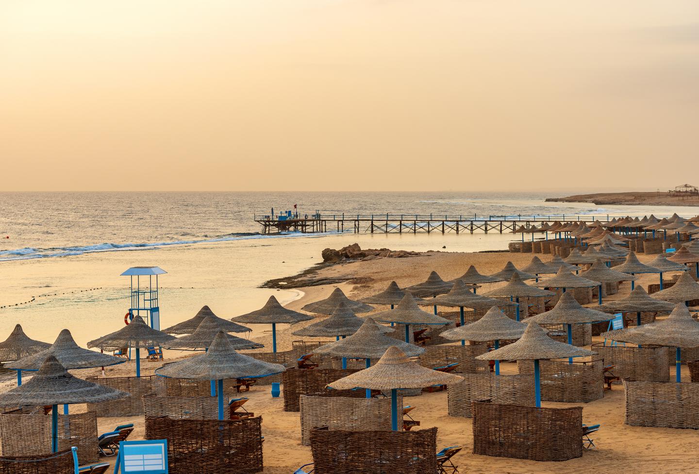 Leerer Sandstrand in der Nähe von Marsa Alam am Morgen mit einem hölzernen Pier über dem Korallenriff zum Tauchen bei Sonnenuntergang.