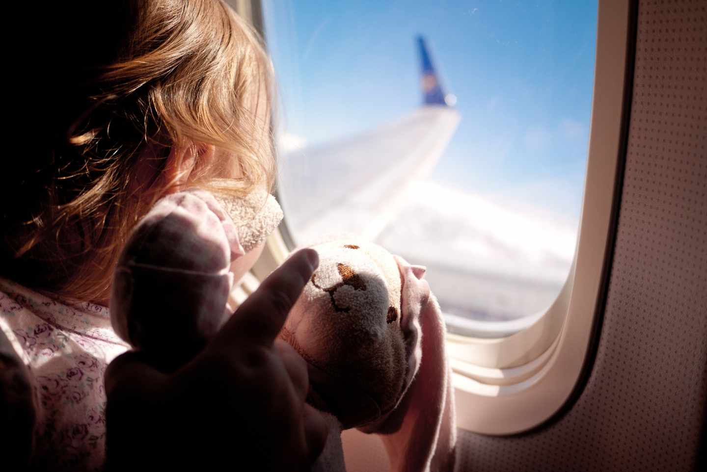 blt4ee831e1af4805c0-kinder-fliegen-baby-flugzeug-teddy-g-171360834.jpg Mädchen mit Teddy schaut aus dem Fenster im Flugzeug