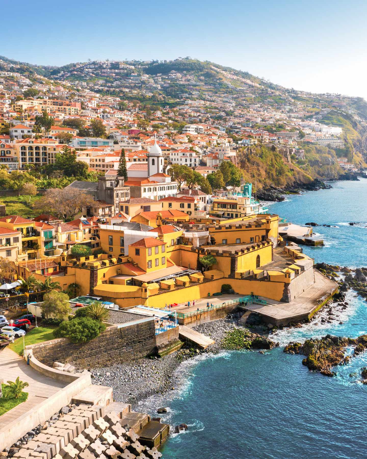 GettyImages-2157681307.jpg Panoramablick auf Funchal mit bunten Häusern am Hang, Atlantikküste und der Festung São Tiago auf Madeira