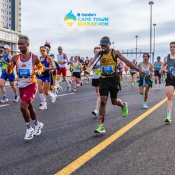 Läufer in bunter Trainingskleidung joggen über eine Brücke in Kapstadt beim Cape Town Marathon