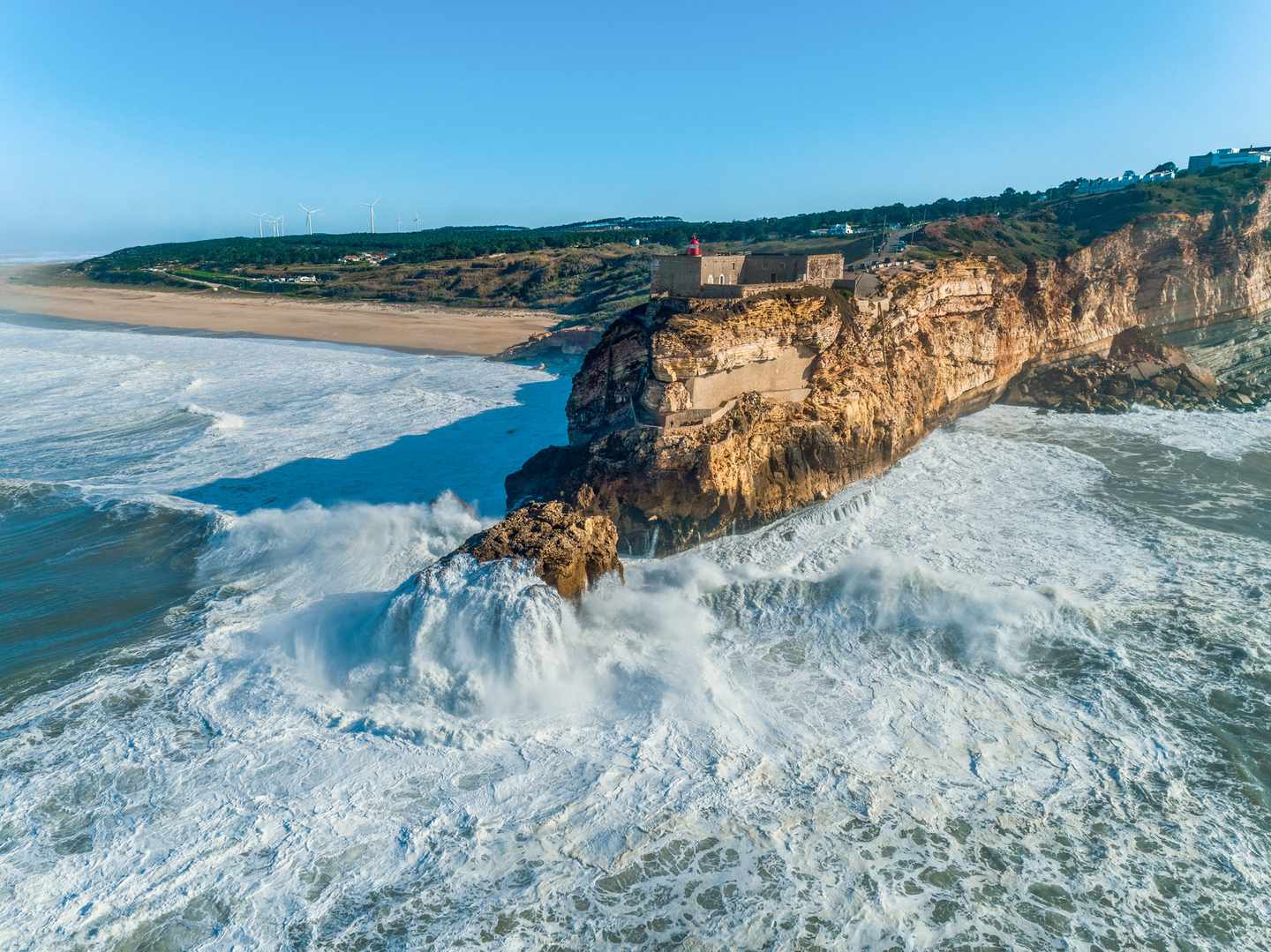 Luftaufnahme des Leuchtturms Forte de São Miguel Arcanjo auf den Klippen von Nazaré mit Atlantikwellen und Steilküste