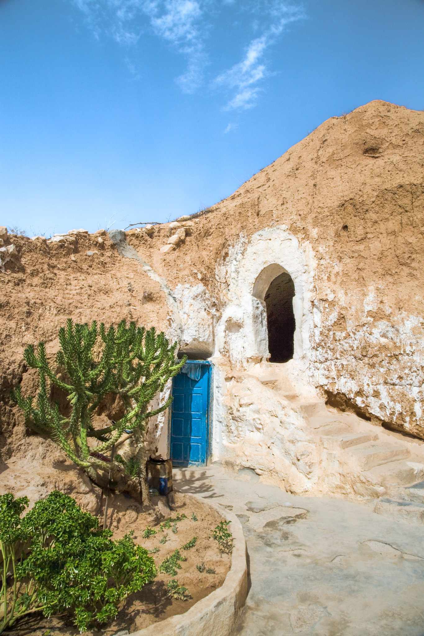 Eingang zu einem traditionellen Troglodytenhaus in Matmata in den Fels gebaut mit weiß verputzter Fassade und blauer Tür