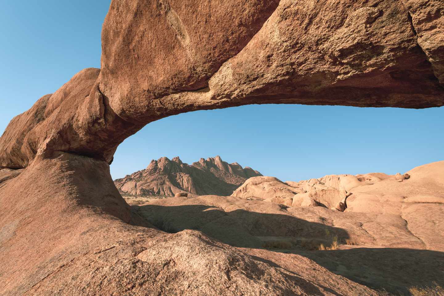 Natürlicher Granit-Felsbogen an der Spitzkoppe mit zerklüfteten Bergen im Hintergrund in Namibia