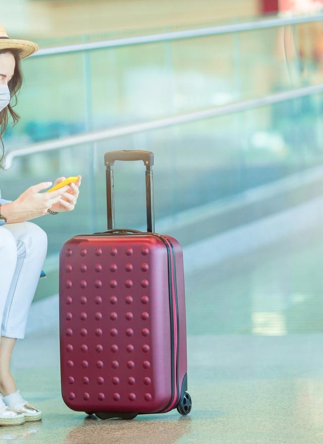 Mehr Informationen Frau mit Maske und Koffer am Flughafen