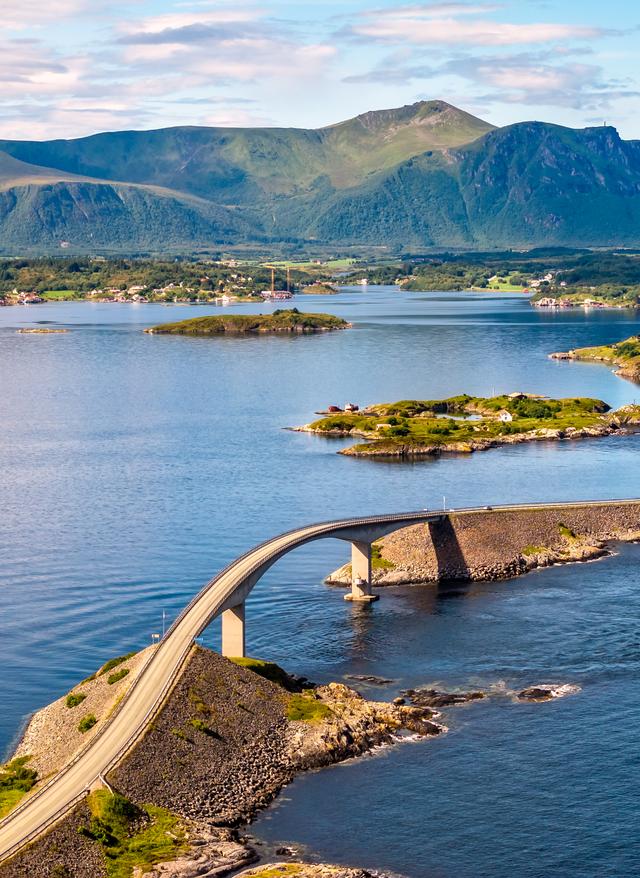 Rundreisen Europa Geschwungene Straßenbrücke verbindet kleine Inseln entlang einer felsigen Küste vor Bergkulisse und Meer