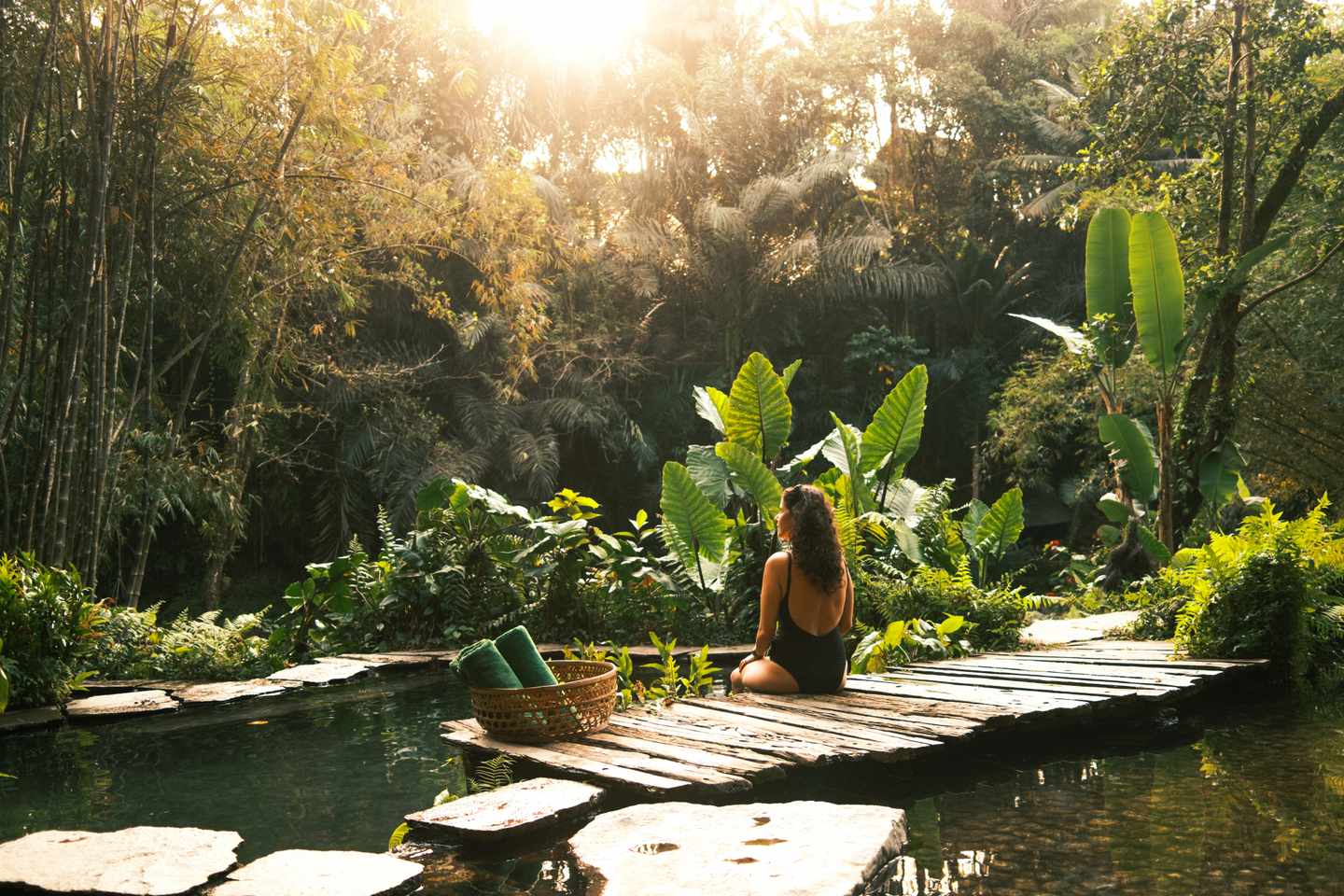 Alleinreisende Frau sitzt an einem Naturpool inmitten dichter tropischer Vegetation und genießt die ruhige Umgebung in Bali