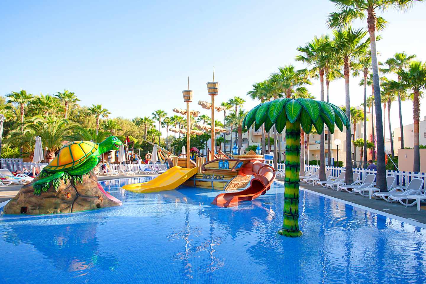 Beste Familienhotels Mallorca – Kinderpool im Hipotels Mediterraneo Club mit Wasserrutschen, Spielschiff und Palmen.