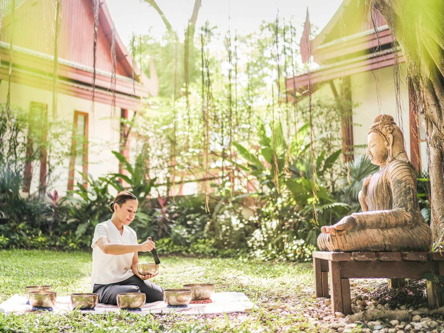 bltc8b6e6f76b8beef5-thailand-nong-kae-frau-klangschale-buddha-h-chiva-som-health-resort-DER1392217.jpg Frau mit Klangschalen sitzt im Grad vor einer steinernen Buddha-Figur