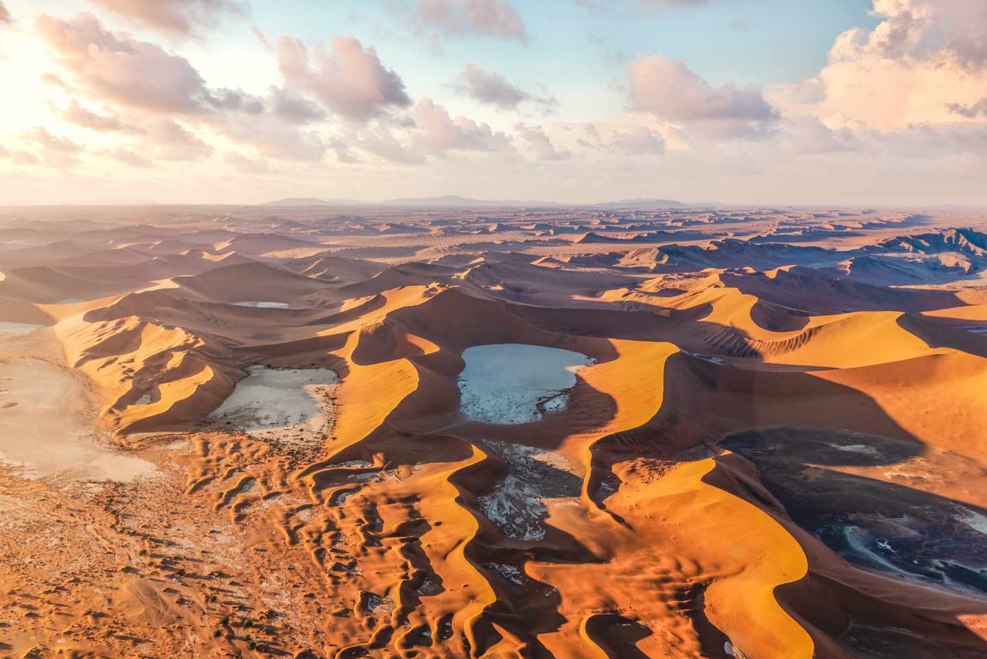 Orangefarbene Dünen und helle Salz-Ton-Pfannen im Sossusvlei aus der Luft bei Sonnenaufgang in Namibia
