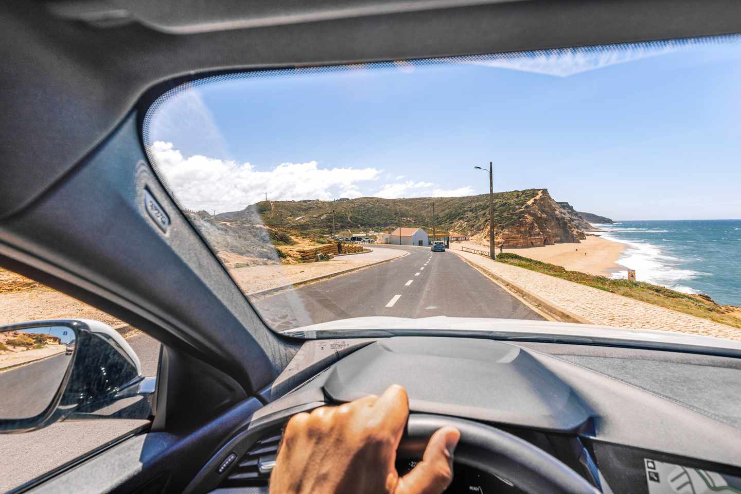 Blick aus einem Auto auf die Küstenstraße entlang der Atlantikküste mit Strand, Felsen und Meer in Portugal