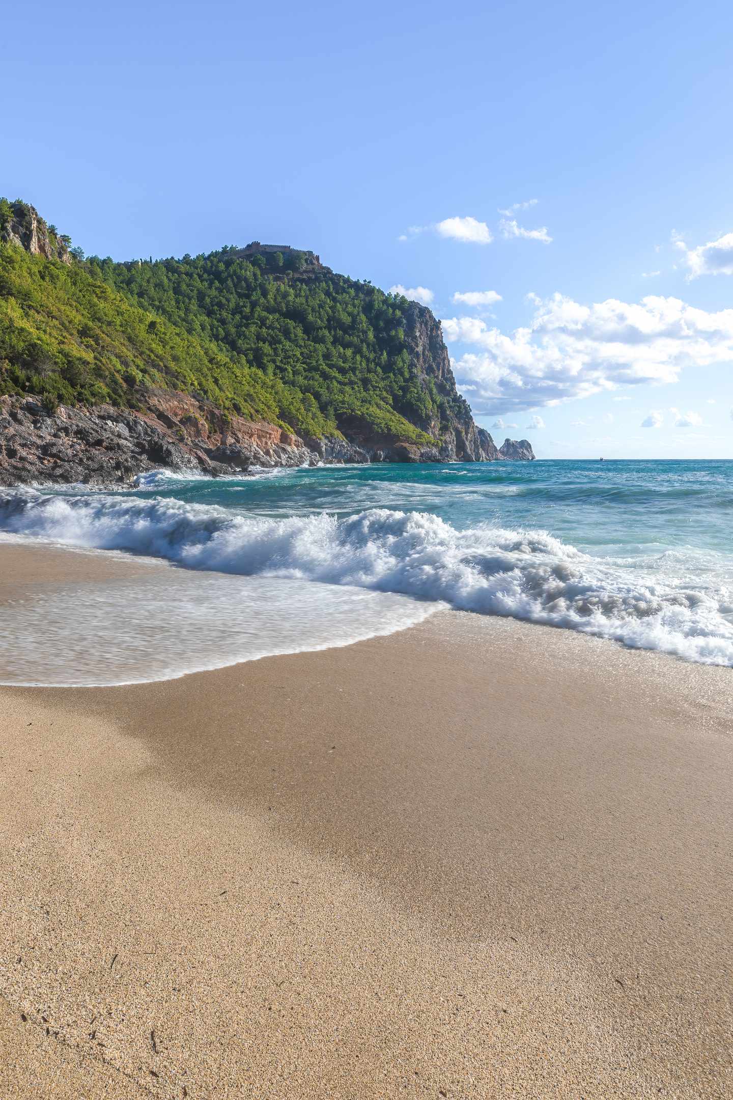 tuerkei-antalya-strand-berglandschaft-g-2241569520.jpg Türkei Urlaub: Sandstrand an der Mittelmeerküste Antalyas mit Wellen und grünen Felsklippen