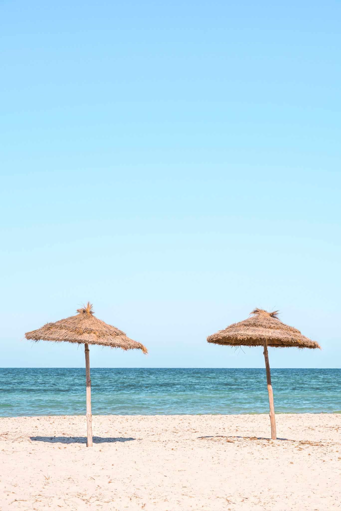 GettyImages-1222581927.jpg Strohschirme am weißen Sandstrand Tunesiens vor türkisblauem Mittelmeer und wolkenlosem Himmel