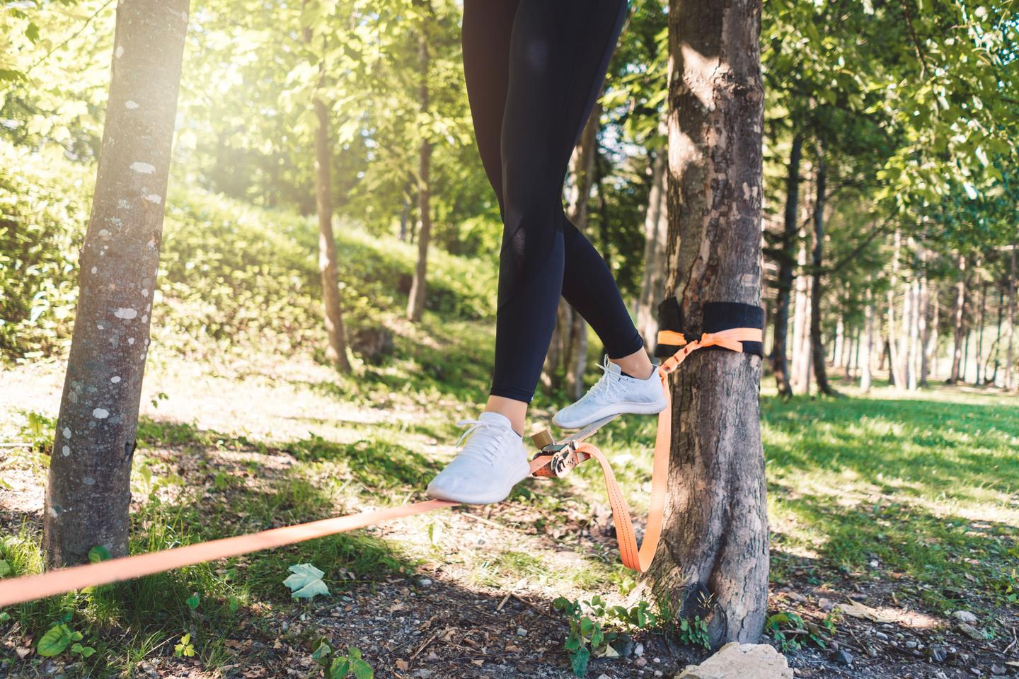 Frau balanciert auf einer zwischen Bäumen gespannten Slackline