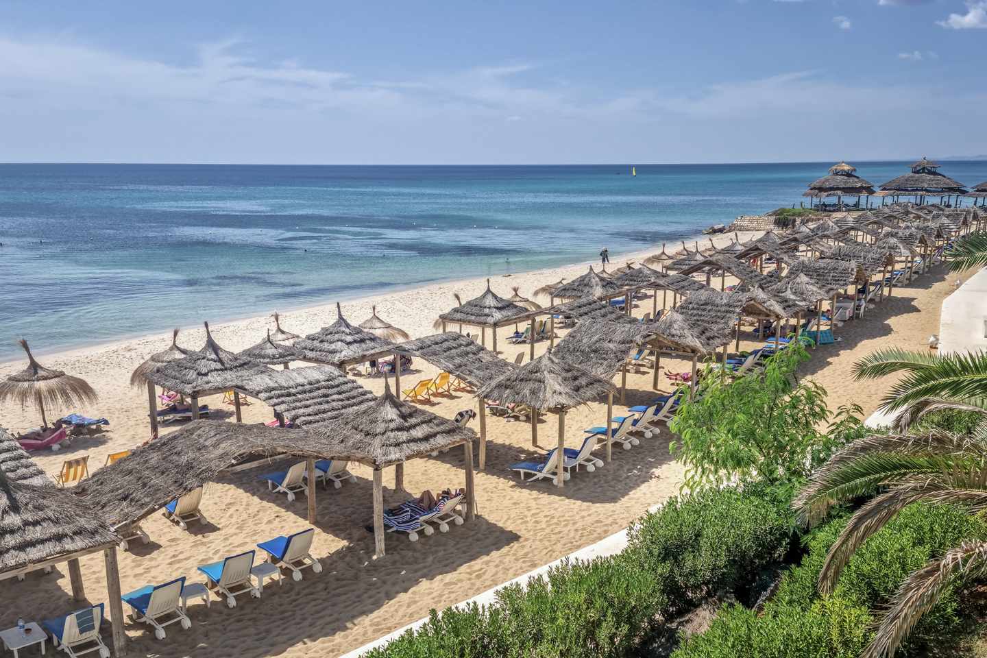 Breiter Sandstrand von Hammamet mit Strohdächern, Liegen und türkisblauem Mittelmeer an der tunesischen Küste