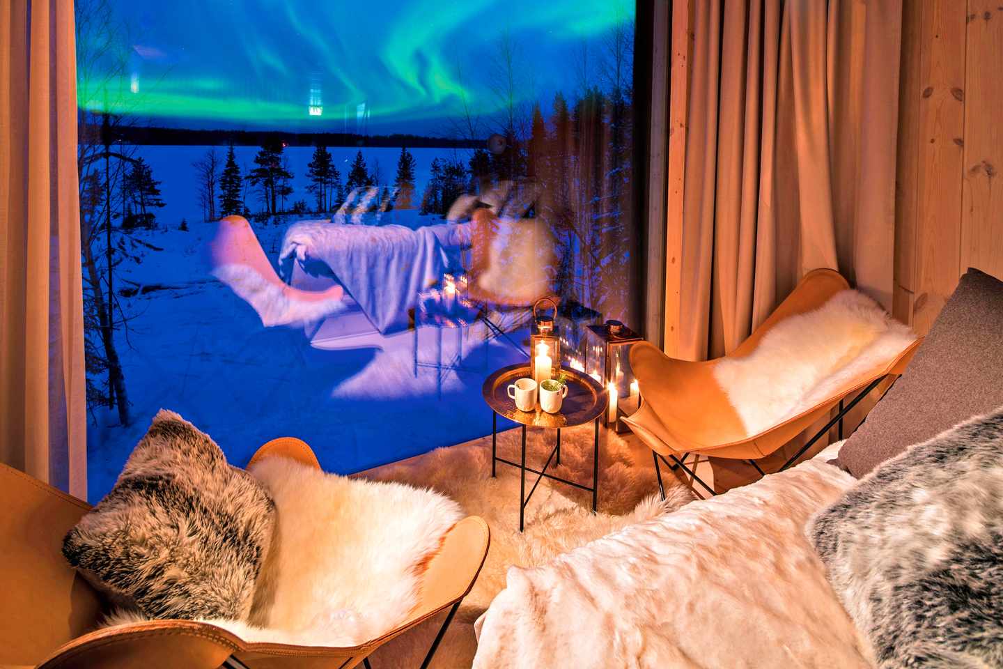 blt84f20201ecd51a91-polarlichter-hotels-Arctic_Treehouse_Hotel-DER1267436.jpg Zwei bequeme Stühle mit Decken vor einem Fenster, dahinter ist es dunkel mit Polarlichtern