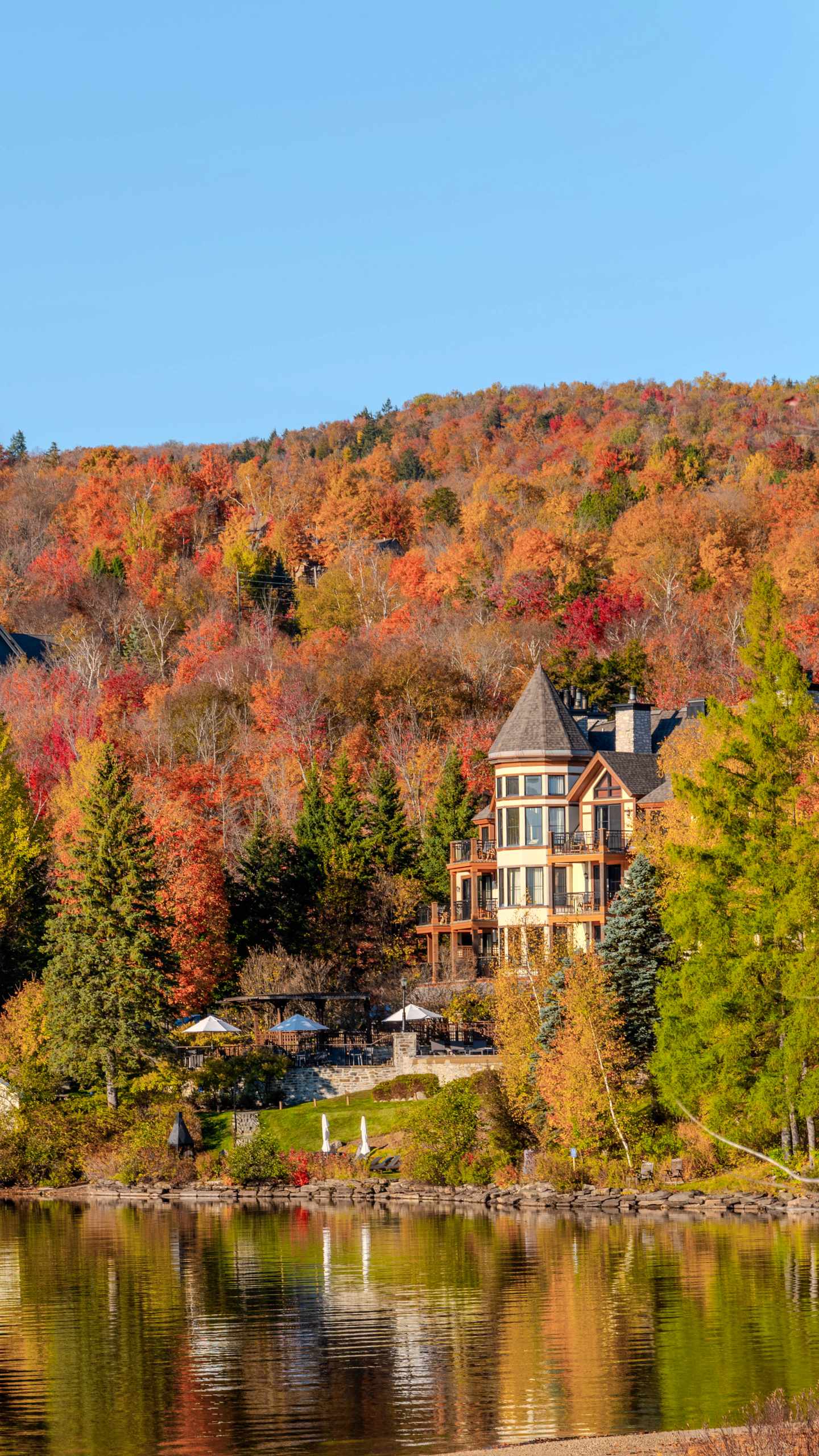 GettyImages-2218647543.jpg Haus am Seeufer vor bunt gefärbtem Herbstwald mit Spiegelung im ruhigen Wasser