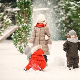 Drei Kinder in Winterkleidung spielen im Schnee zwischen Tannenbäumen
