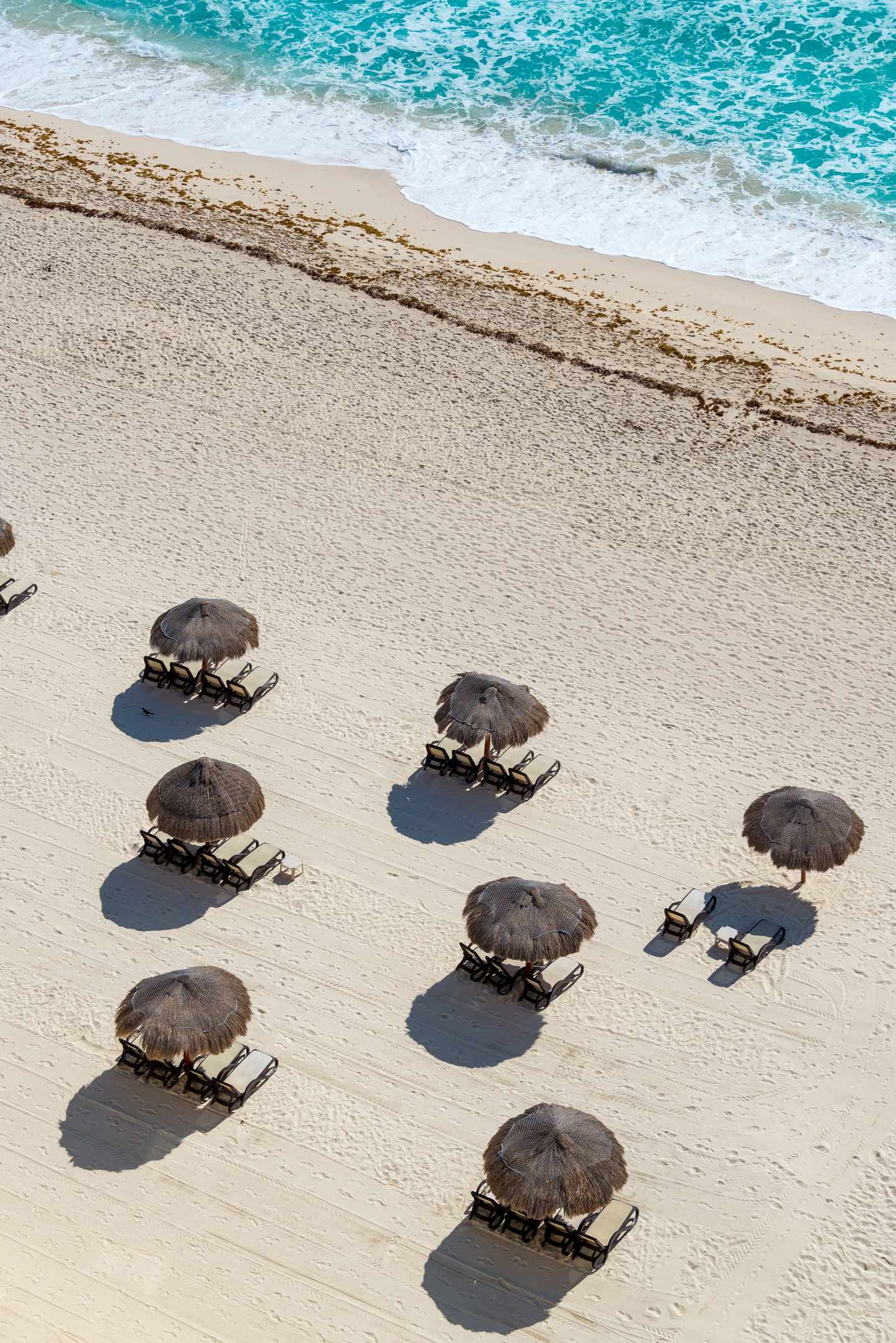 GettyImages-1128055581.jpg Vogelperspektive auf karibischen Sandstrand mit Palmblättern gedeckten Sonnenschirmen
