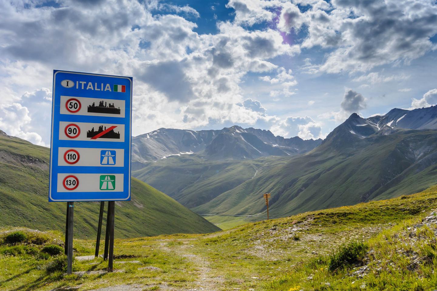 Schild zu Roadtrip-Routen durch Italien vor Bergkulisse