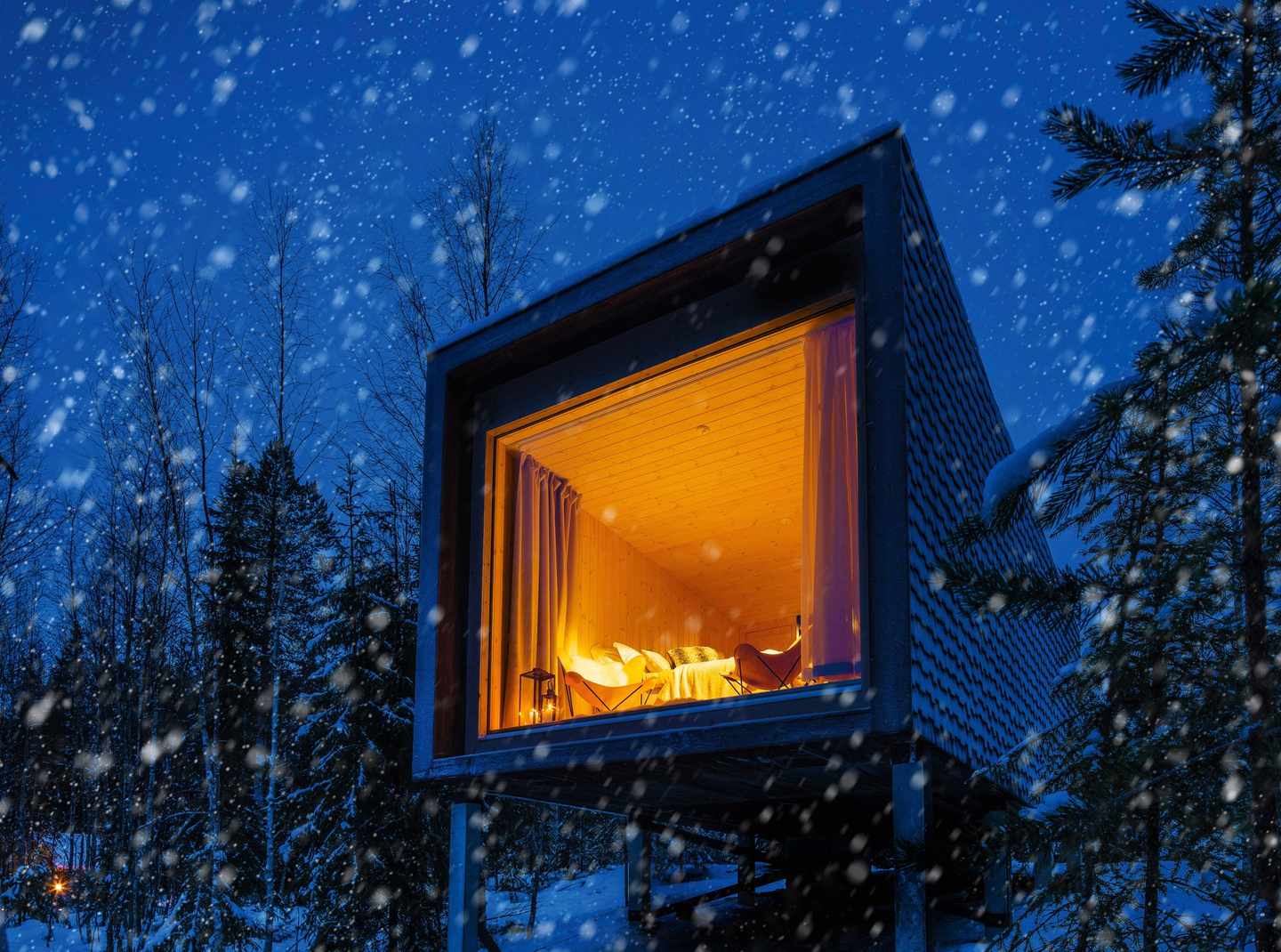 blt1f28e6abbeaa472b-polarlichter-hotels-Arctic_Treehouse_Hotel-DER1267433.jpg Blick von außen auf das Arctic Treehouse Hotel bei Nacht, es schneit, drinnen erleuchtet