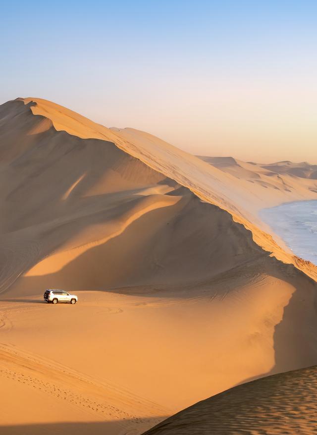 Rundreisen Namibia Gerade Schotterstraße durch goldene Savanne mit den markanten Felsbergen der Spitzkoppe am Horizont in Namibia