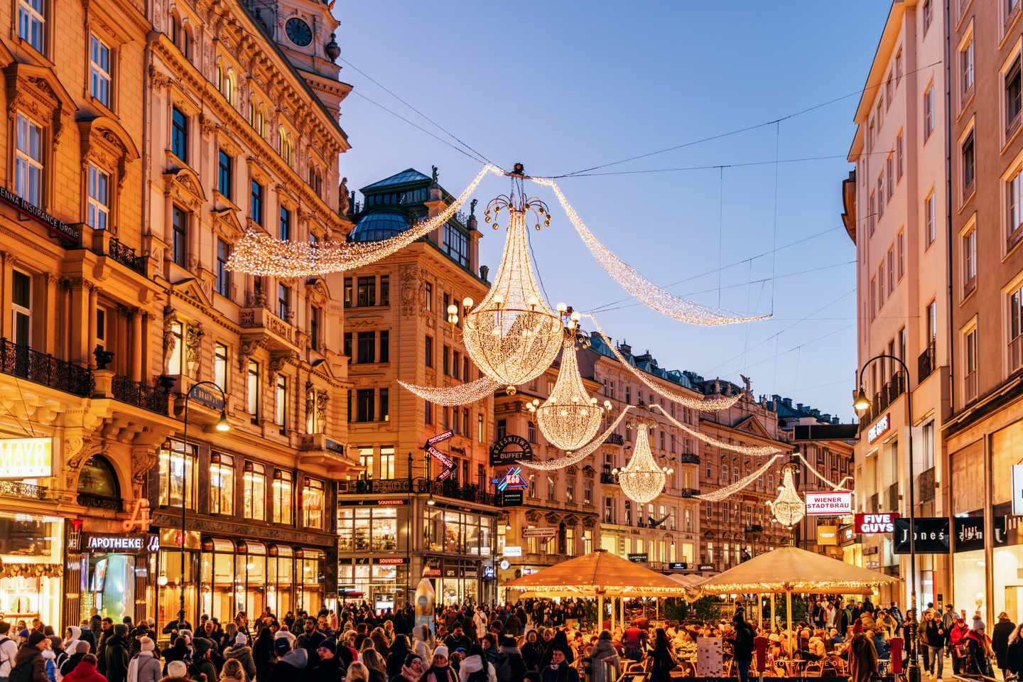 Weihnachtlich beleuchtete Einkaufsstraße in Wien mit großen Kronleuchtern und zahlreichen Besuchern