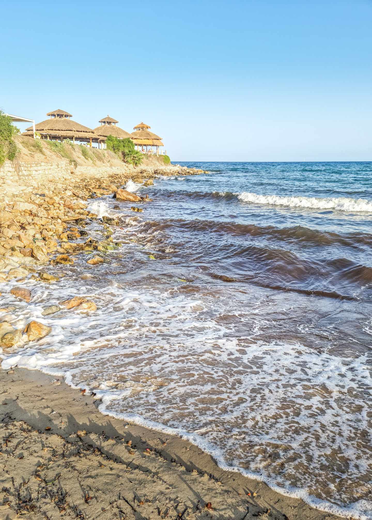 Felsige Küste bei Hammamet mit sanften Wellen, Mittelmeer und Strandrestaurants oberhalb der Uferlinie